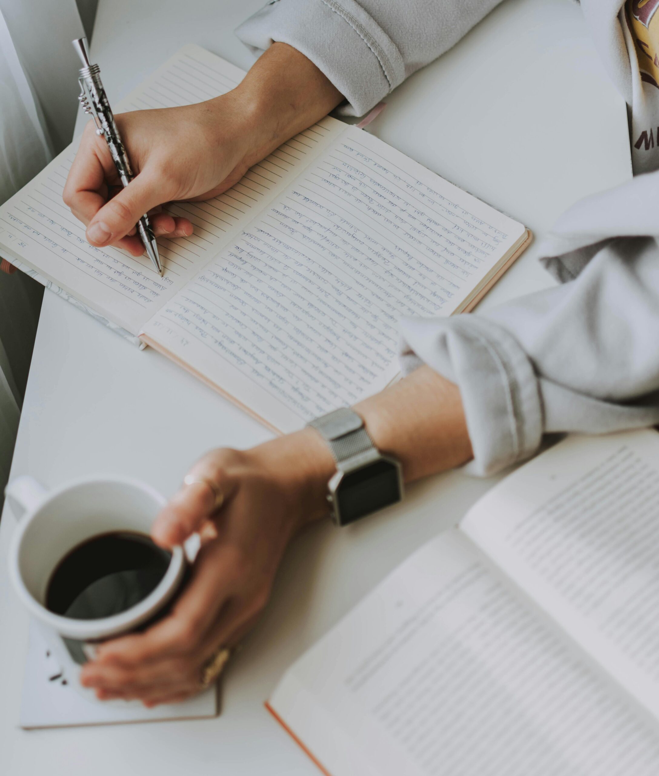 Person writing on notebook while holding coffee mug